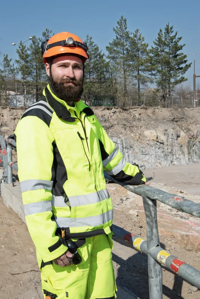 Rakennustyöntekijä Dani Lähde nojaa työmaa-aitaan ja katsoo kameraan.